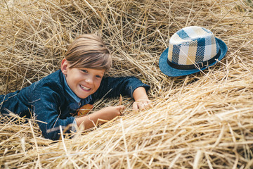 Little boy advertises natural products. The boy advertises children's clothes for the autumn. Portrait of a cheerful boy lying in a hay. Happy child at the autumn fair.