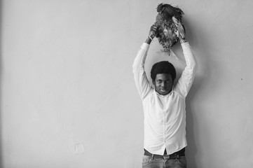 African american man holding chicken above his head in studio. Dark skinned man and his friend - rooster.