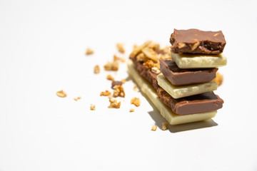 Side view on roughly cut chocolate bars stacked, with granola/ muesli in the background. Brown and white chocolate bars stacked, isolated on white background. Balanced diet concept.