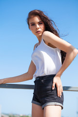 Pretty young brunette model in white summer blouse and jeans, summer street outdoors