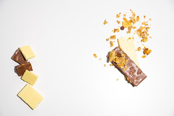 Top view on chopped white/ brown chocolate bars with spilled granola, muesli. Isolated on white background. Empty, copy space on the middle.