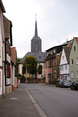 Fototapeta na wymiar Der Turm der Marienkirche in Bischofsheim am Ende einer Hauptverkehrsstraße mit angrenzenden Wohnhäusern...