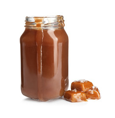 Jar of tasty caramel sauce and candies isolated on white