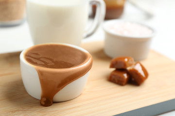 Bowl with caramel sauce and candies on board, closeup