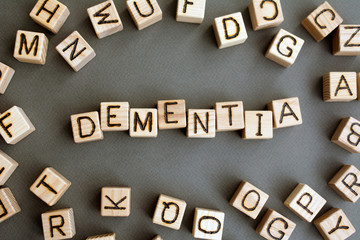 the word dementia wooden cubes with burnt letters, memory loss due to neuronal damage in the brain  gray background top view, scattered cubes around random letters