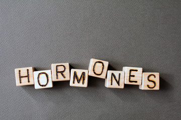 the word hormones wooden cubes with burnt letters, the value of hormones in the human body, gray background top view, scattered cubes around random letters
