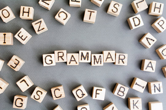 the word grammar wooden cubes with burnt letters, study of grammar of different languages,  gray background top view, scattered cubes around random letters