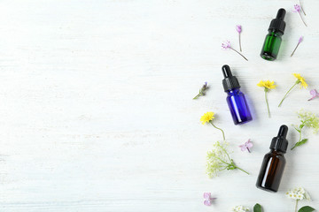Flat lay composition with essential oils and flowers on white wooden table, space for text