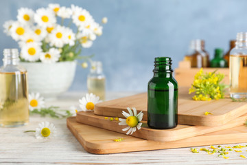 Bottle of essential oil and flowers on wooden table against color background, space for text