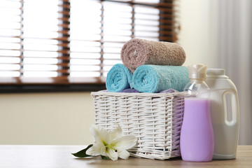 Clean towels in basket with lily and detergents on table indoors. Space for text