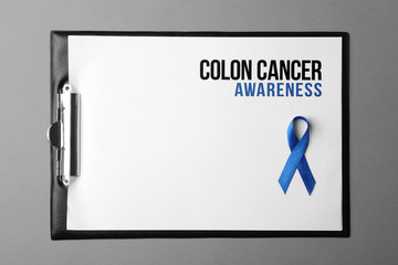 Clipboard with blue ribbon and text Colon cancer awareness on color background, top view