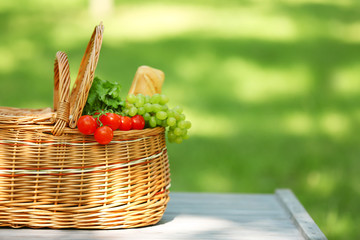 Fototapeta na wymiar Wicker basket with food on table in park, space for text. Summer picnic