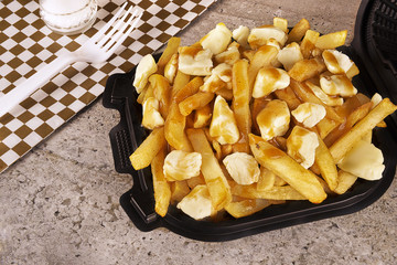 Poutine in a takeout container. Cooked with french fries, gravy and curd cheese. Canadian cuisine.