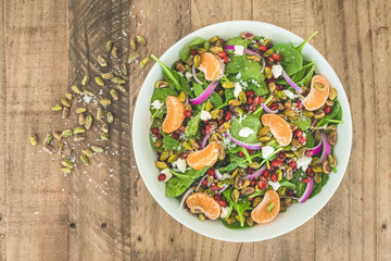 Fresh Gourmet Salad with Fresh Fruit, Raw Pistachio Nuts, and Green Leafs in Rustic Wooden Bowl on Wooden Farm Table