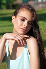 Naklejka premium Young brunette woman in a turquoise blouse posing sitting on a green lawn in a summer park