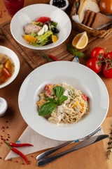 Close up of pasta with vegetables, chicken and creamy sauce, decorated with basil, served on a white table and as a part of set menu