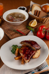 Close up of bbq fried ribs in a spicy sauce with baked potato, served in a white dish and as a part of nutritious set meal in a restaurant
