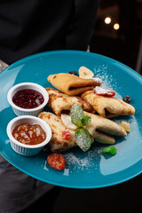 Tattooed waiter is holding a dish with gourmet crepes and marmalade