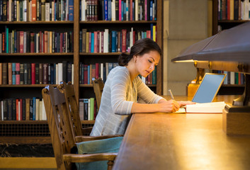 Young woman female college university student with laptop computer studying in library on campus