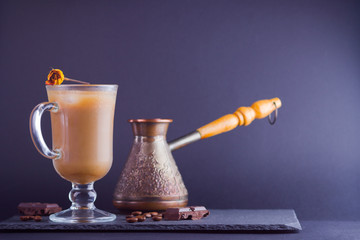 Copper coffee pot (Cezve) and coffee beans. Coffee with milk on dark background. Latte and black chocolate on slate board. Milk drink in glass beaker and dried rose