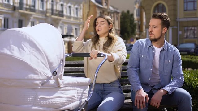 Upset mom worrying about crying baby pram, indifferent husband sitting on bench