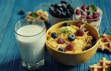 Tasty cornflakes with raspberries and blueberries on blue background. Wafers and milk. A great start to the day.