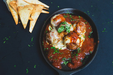 Albondigas de ternera con una salsa pomodoro gratindos con queso emmental  en un sarten sobre un fondo negro