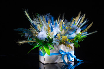 wooden box with beautiful spring floral bouquet decorated with feathers on black background 
