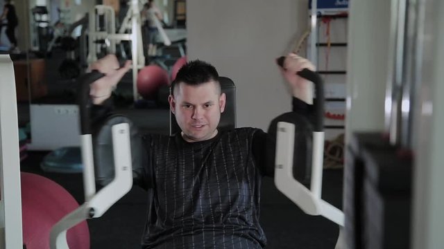 Adult man with excess weight trains his chest on the simulator.