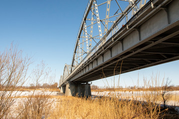 Metal arches of the bridge over the river. Winter, landscape.