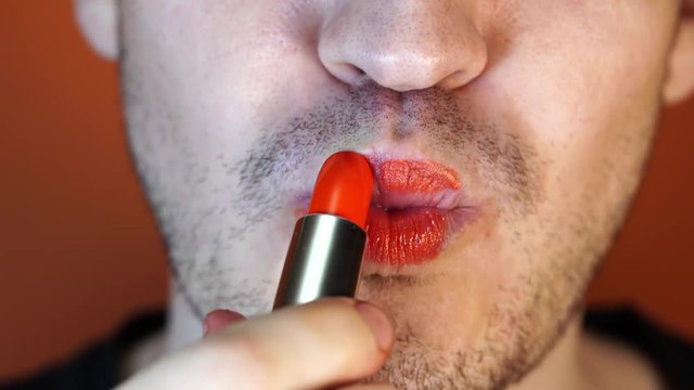 Man paints lips with red lipstick, close-up.