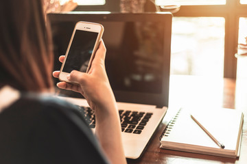 Close-up of business female working with smartphone and laptop in coffee shop like the background.