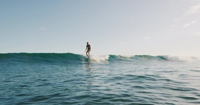 Young woman surfing a wave in slow motion, smiling and walking to the nose of her longboard to hang five on summer wave at sunset