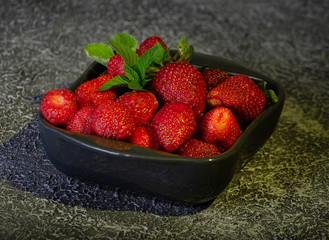 ceramic dark plate with ripe strawberries decorated with mint leaves