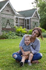 Young mother and toddler son sitting in grass during summer smiling and laughing