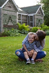 Young mother and toddler son sitting in grass during summer smiling and laughing