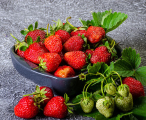 ceramic plate with ripe strawberries decorated with mint near sprig of strawberries on a dark background place for advertising