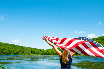 4th of July. Young woman holding American flag on lake background.