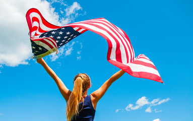 Young woman holding American flag on blue sky background.