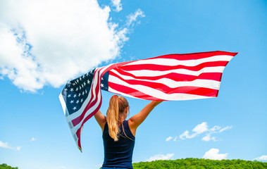 Young woman holding American flag on blue sky background. United States celebrate 4th of July