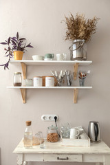 Pots with various houseplants and assorted dishware standing on shelf and cupboard in cozy kitchen