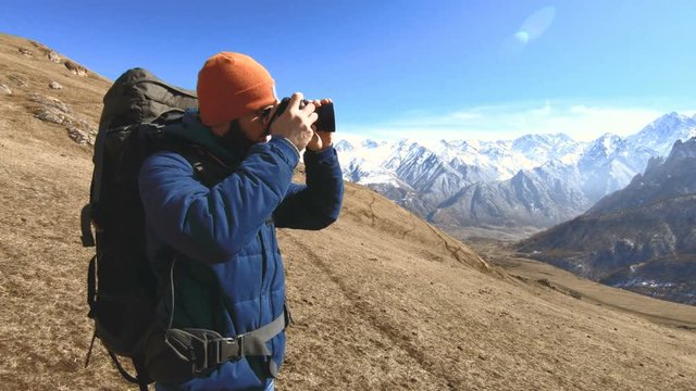 Portrait of a happy bearded traveler photographer in sunglasses and a hat with a reflex camera in his hands and taking pictures against the background of the mountains. Photo travel concept