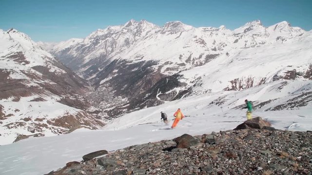 Skiers ski down a valley into a small mountain village below