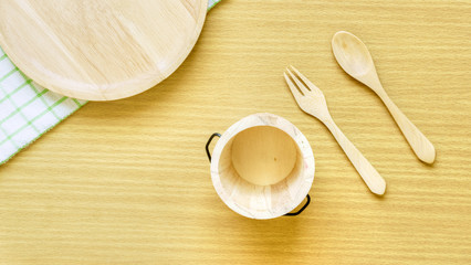 Top view closeup set of wooden cutlery utensil. Wooden fork, spoon, plate and bucket on wooden table background. Clean green and white checkered pattern hand towel on wooden table.