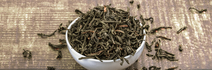 Dried tea is poured into a ceramic cup on a wooden plank table.