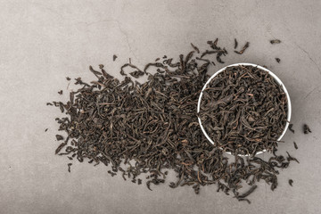 Dried tea is poured into a white ceramic cup on a gray textured background. View from above. Layout.