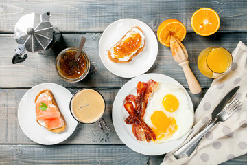 The English breakfast - eggs,  bacon,  toasts with ricotta and jam, juice in a glass, coffee on a grey background. Top view.