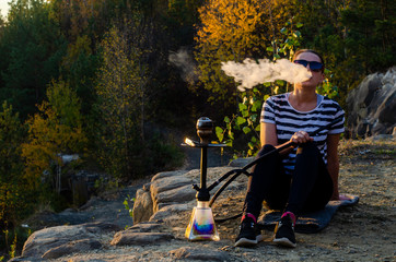 A woman smoking shisha (hookah) sitting by the sea. Seagulls at the background.