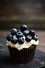 Homemade muffin with blueberry and cream cheese frosting on the rustic background. Selective focus.
