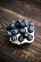 Homemade muffin with blueberry and cream cheese frosting on the rustic background. Selective focus.